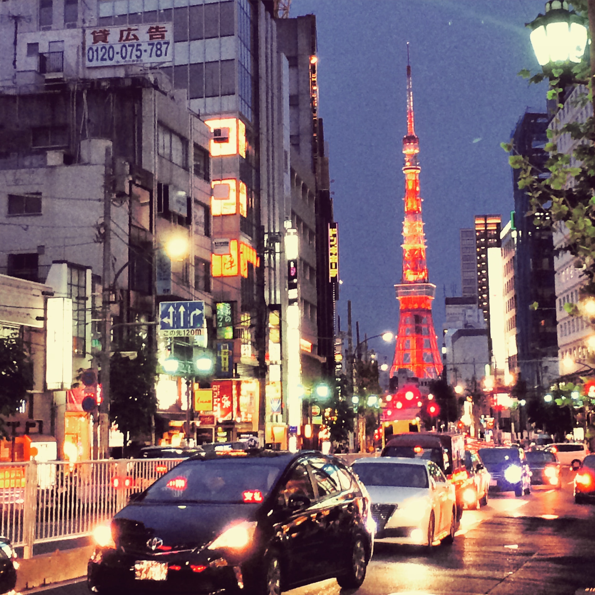 Tokyo Tower lit up at dusk above a busy Tokyo street