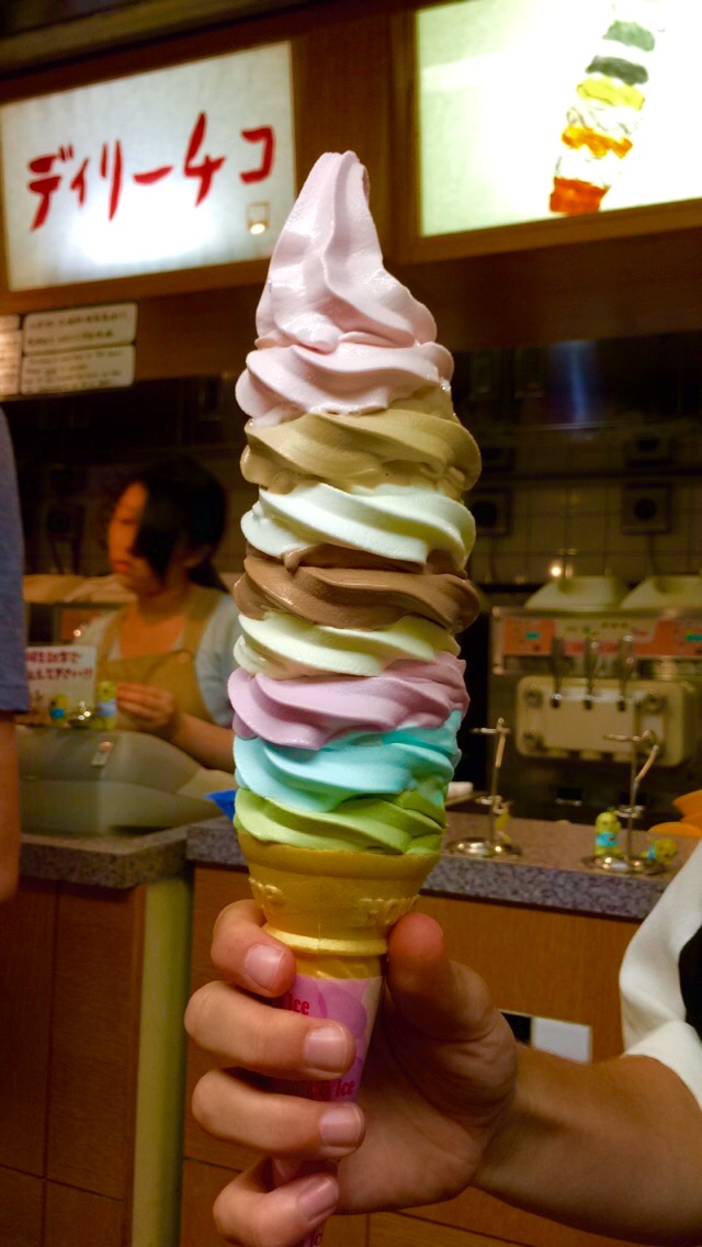 A tall rainbow soft-serve ice cream cone held up in a shop in Japan